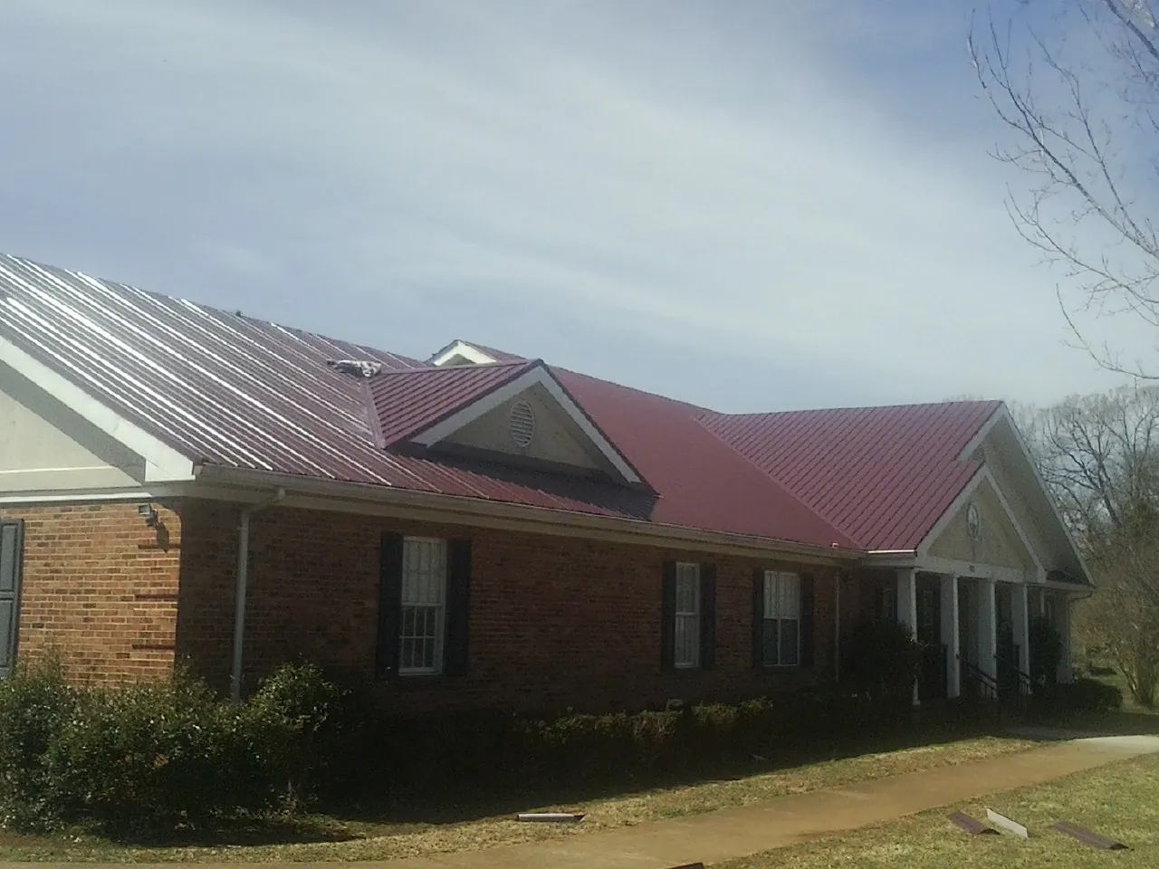 Red metal roof with gabled entries on a long brick building, from a Hail Damage Roof Repair job in Palm Springs