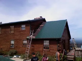 Green metal roof going on a two story log home with ladders set in Palm Springs